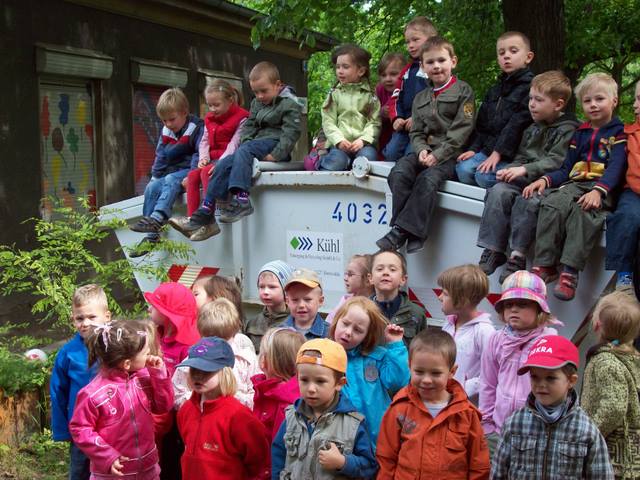 Kinder einer Kita sitzen auf und vor einem Kühl-Container